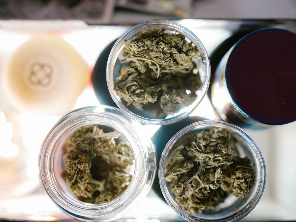Dried cannabis buds curing in open glass jars, seen from above